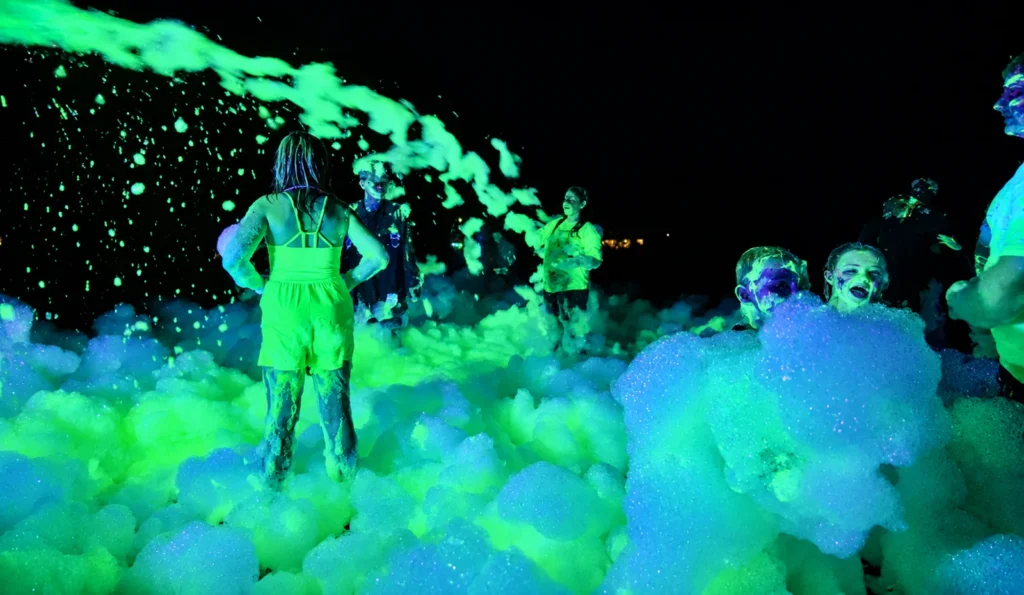 Campers playing in foam under colorful lights at a nighttime activity