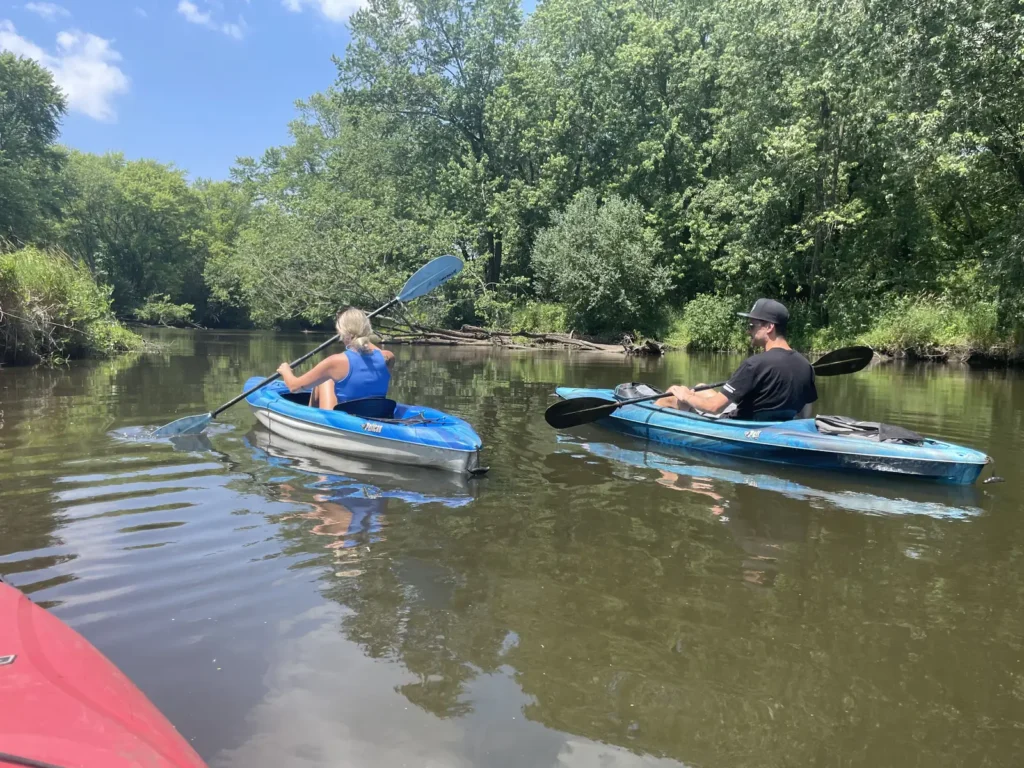 Two kayakers paddling beside the wooded bank of the Kishwaukee River